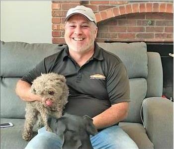 smiling man with a Servpro shirt on sitting on a couch with a dog