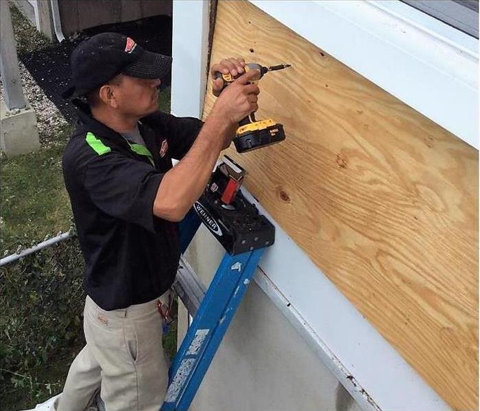 Man boarding up a window after a storm